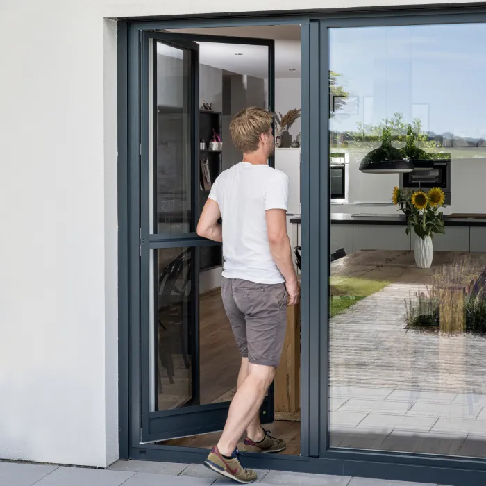 Person geht durch Terrassentür mit Fliegengitter Drehtür als Insektenschutz nach Maß