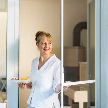 Frau trägt Teller mit Speisen durch eine geöffnete Fliegengitter Schiebetür mit weißem Rahmen