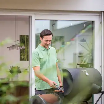 Mann grillt vor der geöffneten Fliegengitter Schiebetür mit weißem Rahmen am Haus