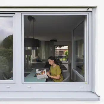 Frau sitzt am Esstisch hinter einem eingesetzten Fliegengitter Spannrahmen im Fensterrahmen